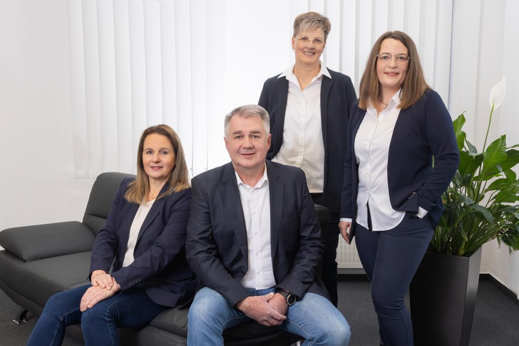 Mehrere Mitarbeitende von Freund Immobilien stehen bzw. sitzen auf einer Couch im Büro und blicken in die Kamera.