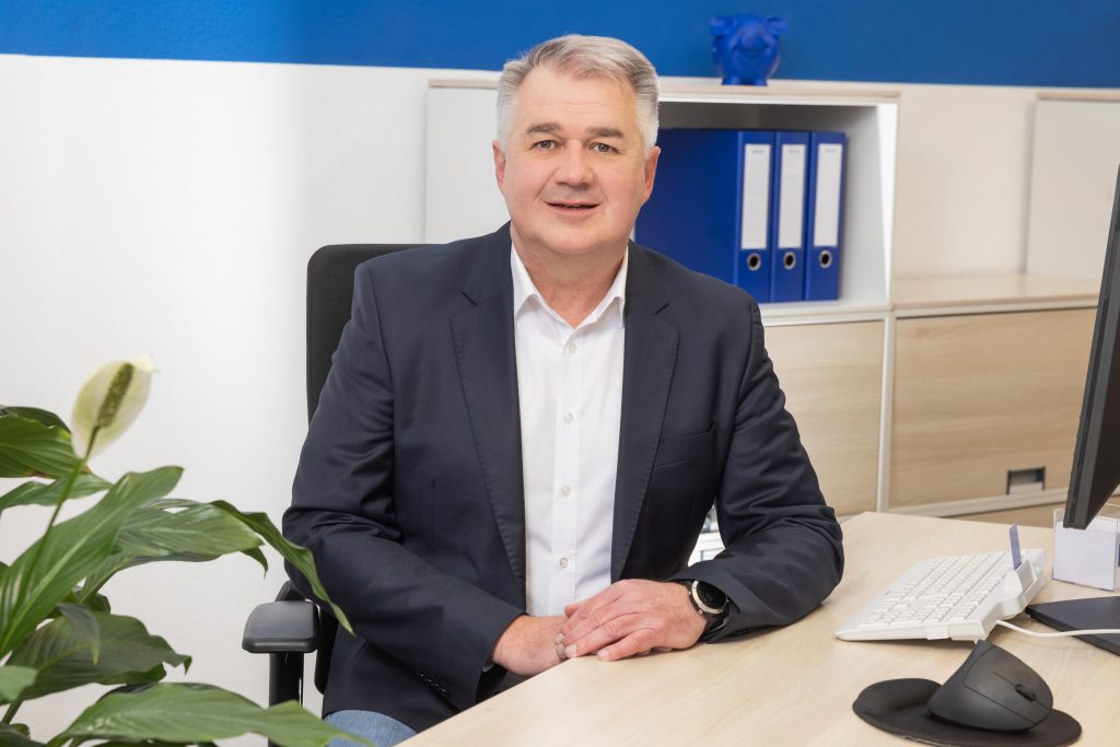 Porträt von Michael Freund, Inhaber von Freund Immobilien, sitzend an einem Schreibtisch in einem Büro und freundlich in die Kamera lächelnd